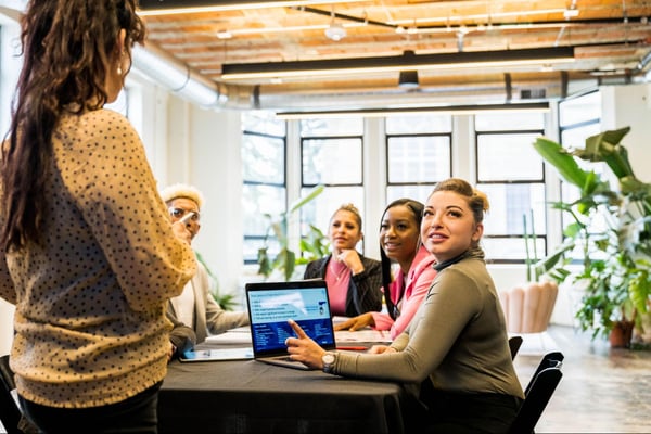 A person standing at the head of the desk with a group of people listening to them